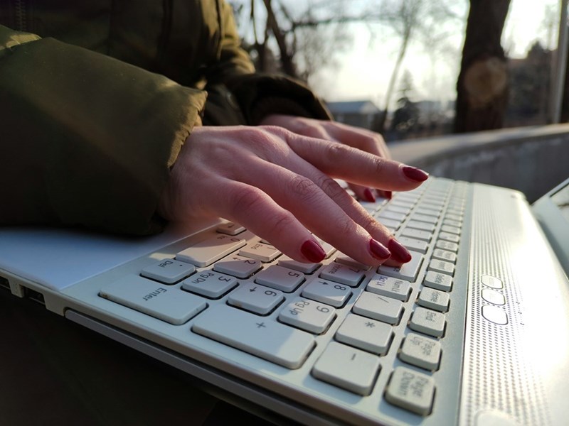 Woman typing outside in the cold on her laptop with painted nails
