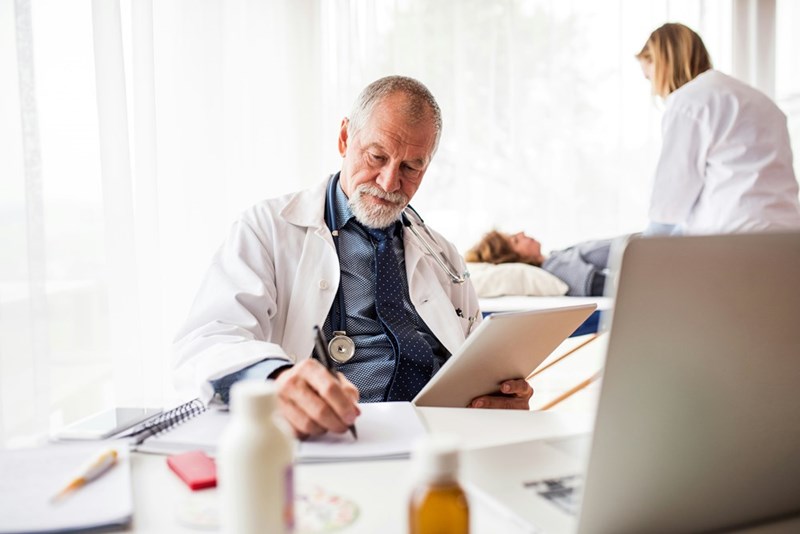 Senior doctor with tablet in his office writing