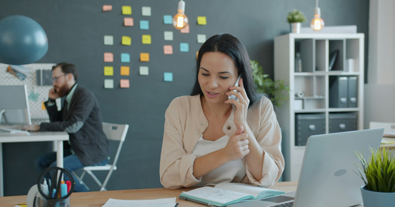 A female employee talks on her cell phone while sitting in an open-plan office