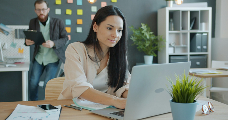 A female employee works on a laptop in an open-plan office