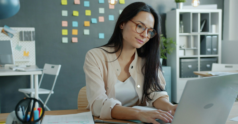 A female employee wears glasses as she works on her laptop in an open-plan office