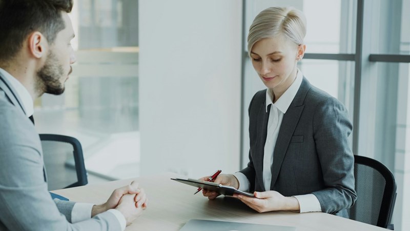 A Human Resources representative scans a document as she meets with a male employee in a conference room.