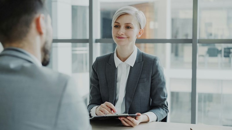 A Human Resources representative smiles at an employee while holding a clipboard.