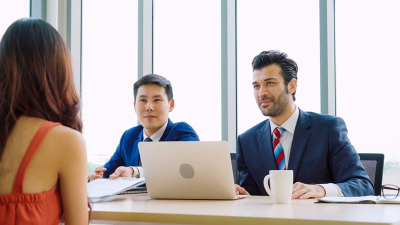 The manager and his employee sit across from a female coworker in a conference room.