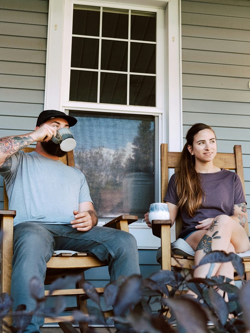 A portrait of a husband and wife, new to their neighborhood, sitting on the front porch of their home.