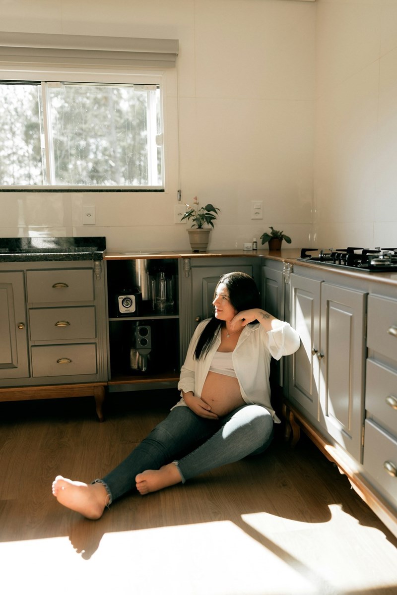 A pregnant woman sits on her kitchen floor, taking a rest