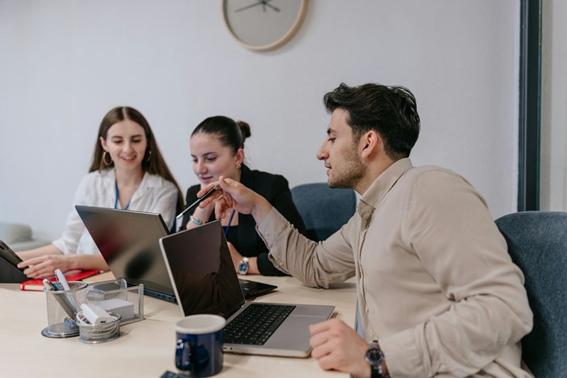 Team of coworkers discussing ideas and working together on laptops in an office meeting.