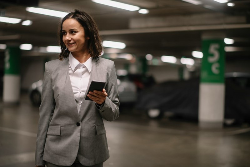 Professional woman holding smartphone while walking through indoor parking garage.