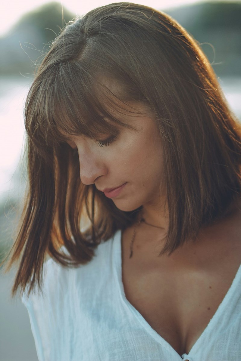 Woman with short brown hair in a white blouse looking down outdoors in soft golden-hour lighting.