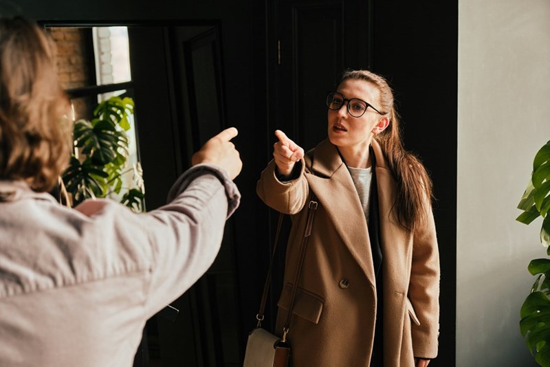 Two women point at each other while shouting in anger