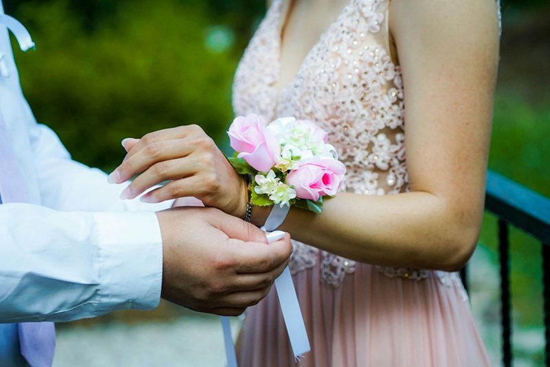 A well-dressed young man gives his prom date a corsage for the dance