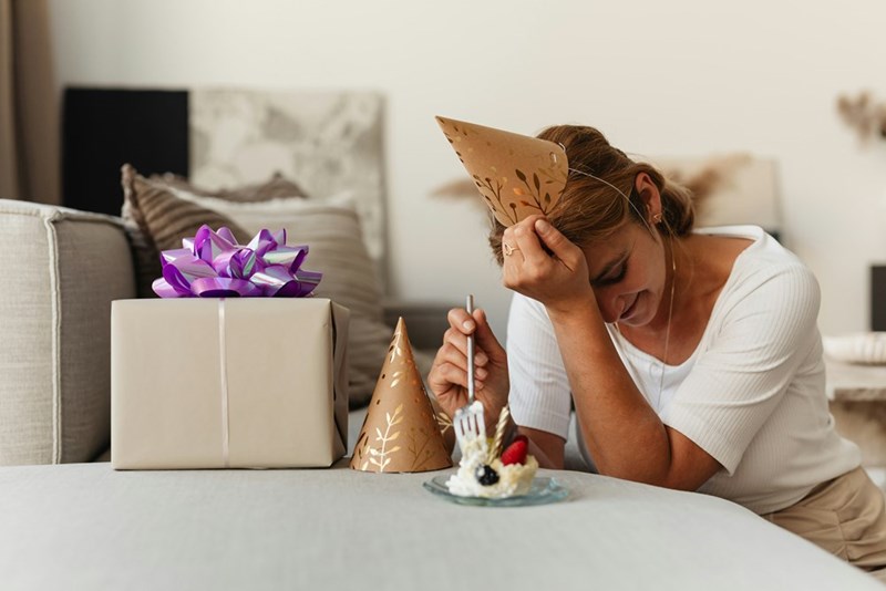 An upset woman sits at a table on her birthday eating cake