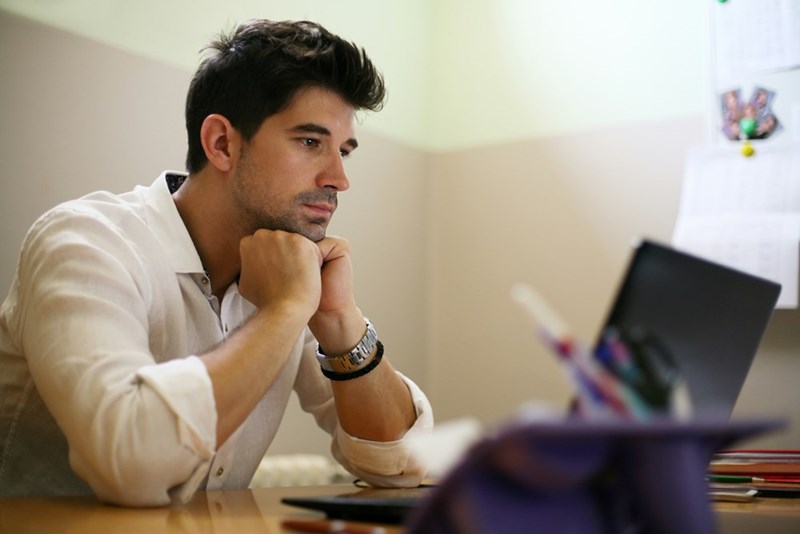 A young professional looks disappointed as he reads emails on his computer.