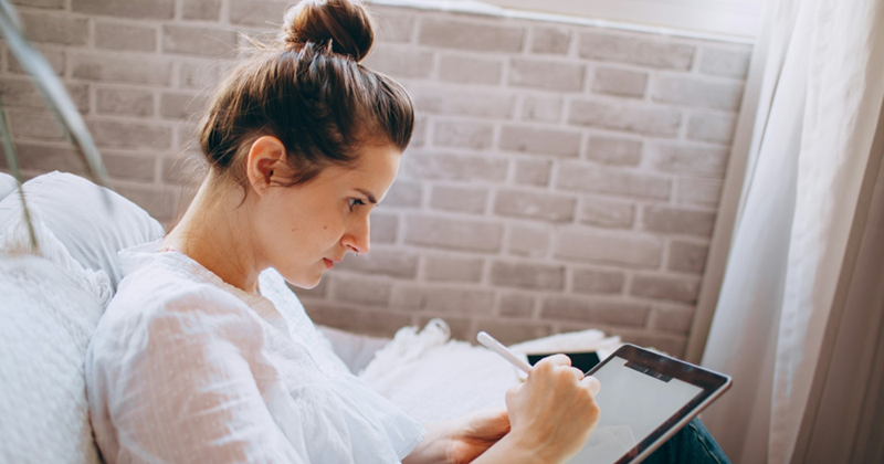 A woman draws on a tablet while sitting on a couch
