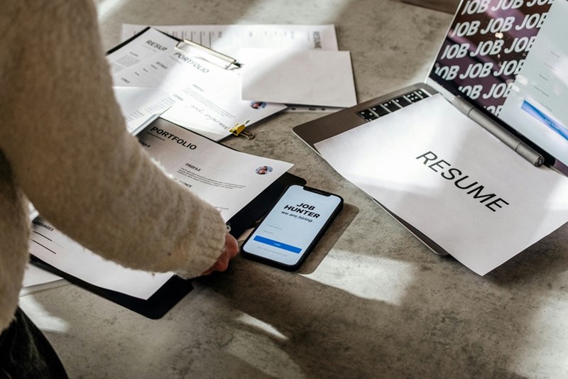 A recruiter reviews a stack of resumes and portfolios on their desk.