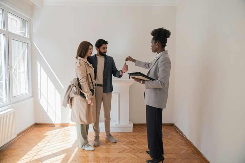 A seller handing over a house key to potential buyers during a property discussion.