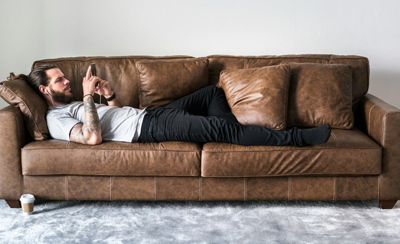 A laid off worker laying on the sofa reading a message on social media from the person who got his job .