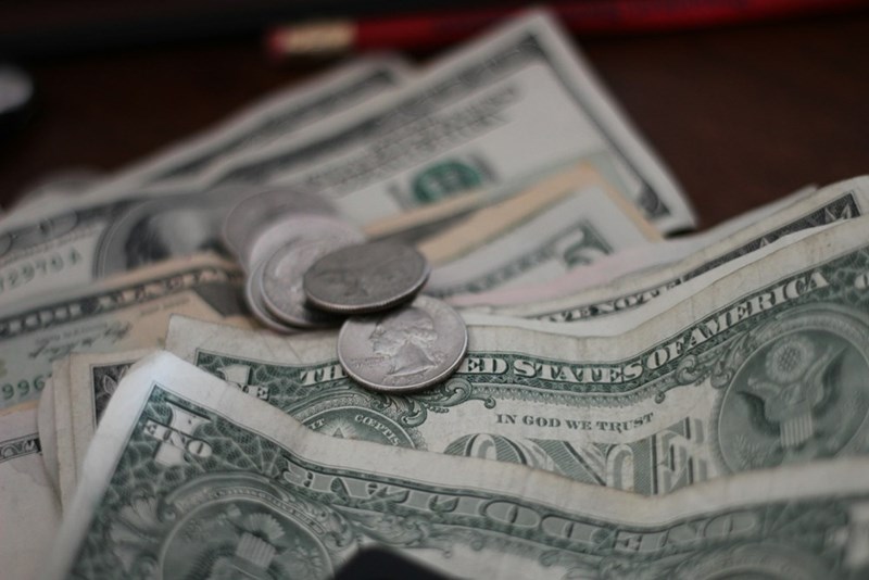 Close-up of U.S. dollar bills and coins scattered across wooden surface.