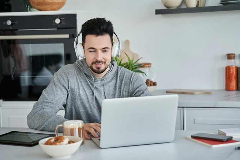 A man wearing headphones sit in front of a laptop