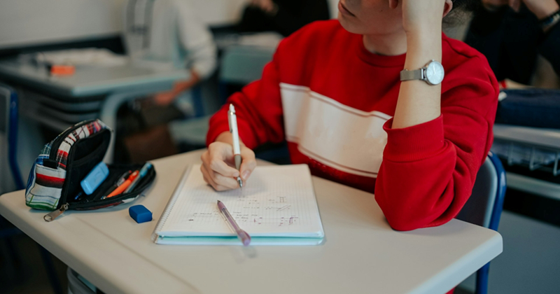 Close-up of a student writing in a notebook while sitting at a desk