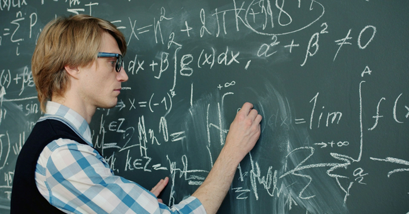 A math teacher writes equations on a chalkboard