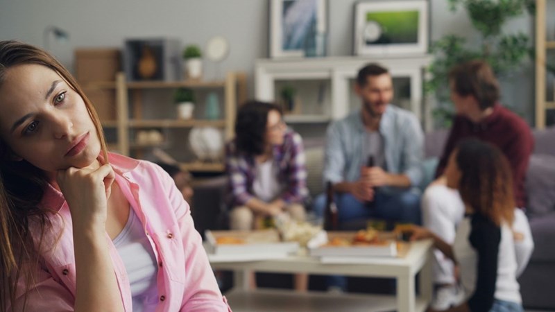 Upset woman laying her head on on a wall with blurred people behind her.