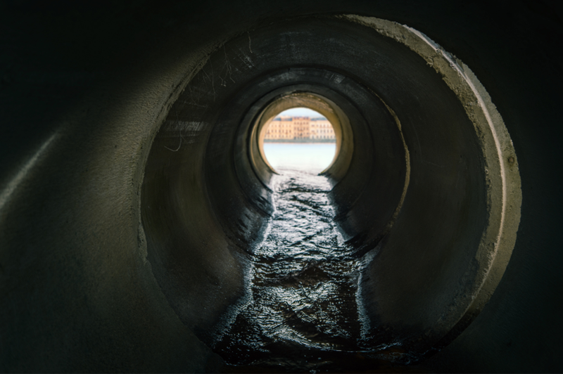 Inside a drain pipe, water is flowing away from the camera towards the exit.