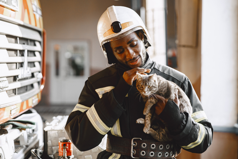 A firefighter holding a cat, looking at it happily.