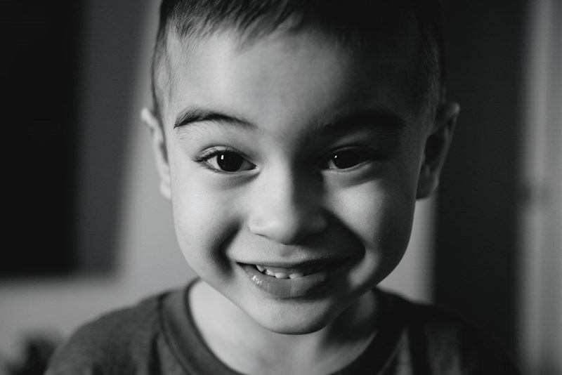 Black-and-white close-up portrait of a smiling young boy looking directly at the camera.