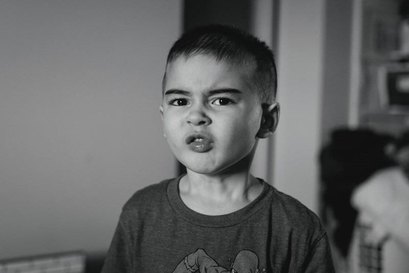 Black-and-white portrait of a young boy making a rebellious facial expression indoors.