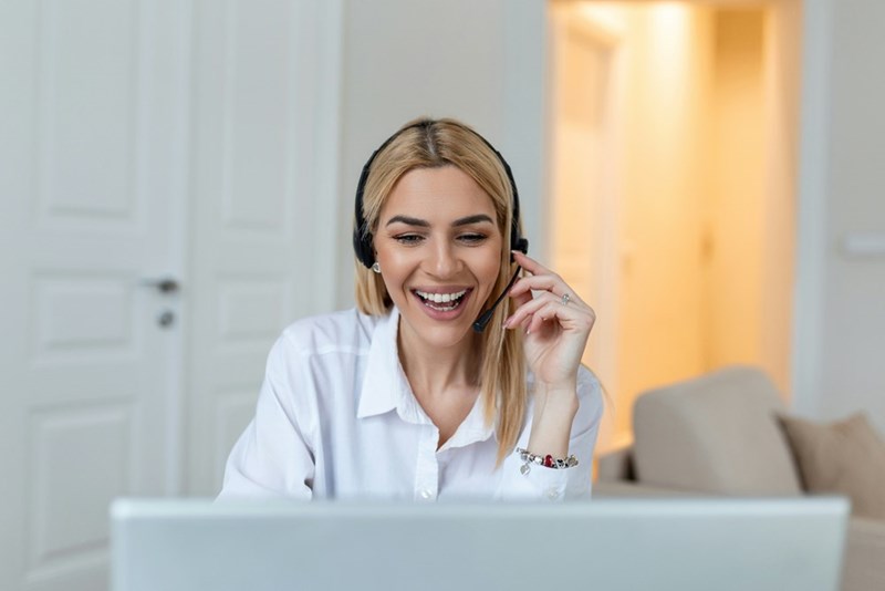Woman sitting down on facing her computer wearing headphones and smiling.
