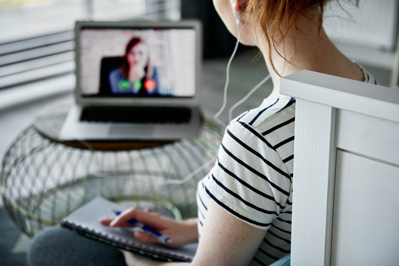 Woman wearing wired earphones looking at her computer while on a zoom call.