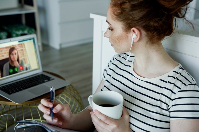 Red haired woman wearing wired headphones looking at her computer while on a zoom call.