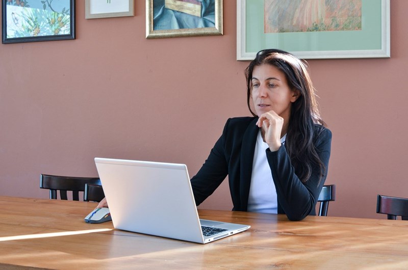 Woman sitting on a desk with a striped shirt looking at her computer.