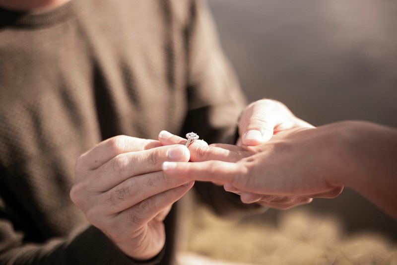 Man proposing to woman putting a ring on her finger.
