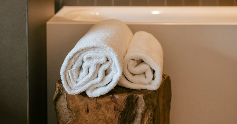 A pair of white towels rolled up on a wooden stand by a bathtub