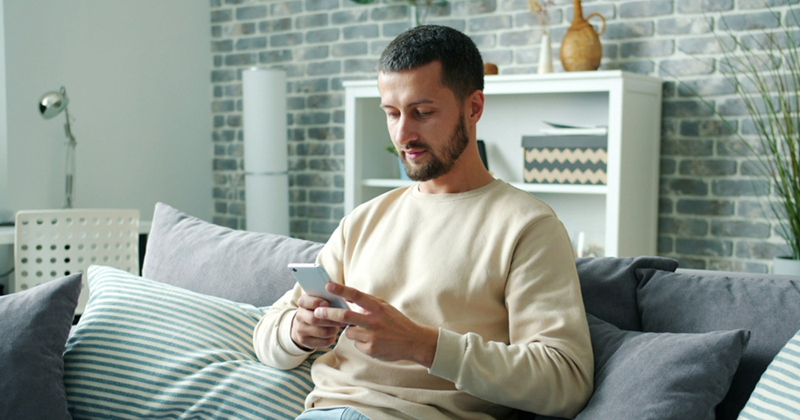 A man sits on a couch and looks at his phone