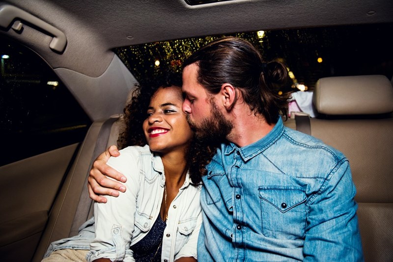 Man kisses his date on the cheek as they take a car ride together.