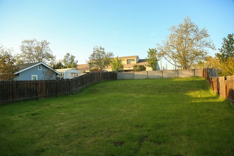 Big grass backyard surrounded by a fence.