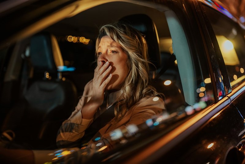 Woman sitting in a car at night covering her mouth with her hand while looking shocked.