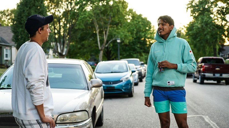 Two men talking on the side of the street wearing casual clothes.
