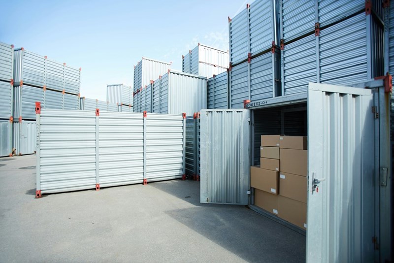 A depiction of an outside storage area with stacked shipping containers, one of which is open and full of cardboard boxes.