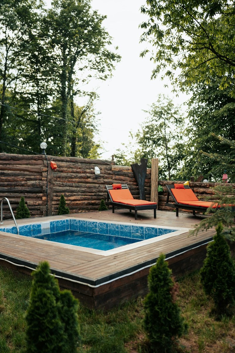 A side view of a neighborhood backyard showing an above-ground pool and lounge chairs.
