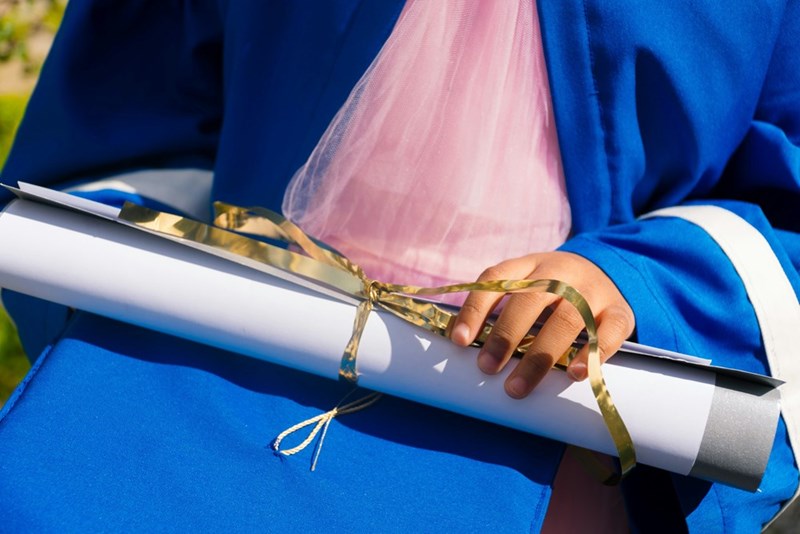 A photograph of a model in a blue gown, clutching her high school diploma.