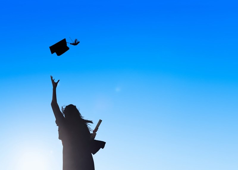 A silhouette of a high school student tossing her graduation cap against a blue sky.