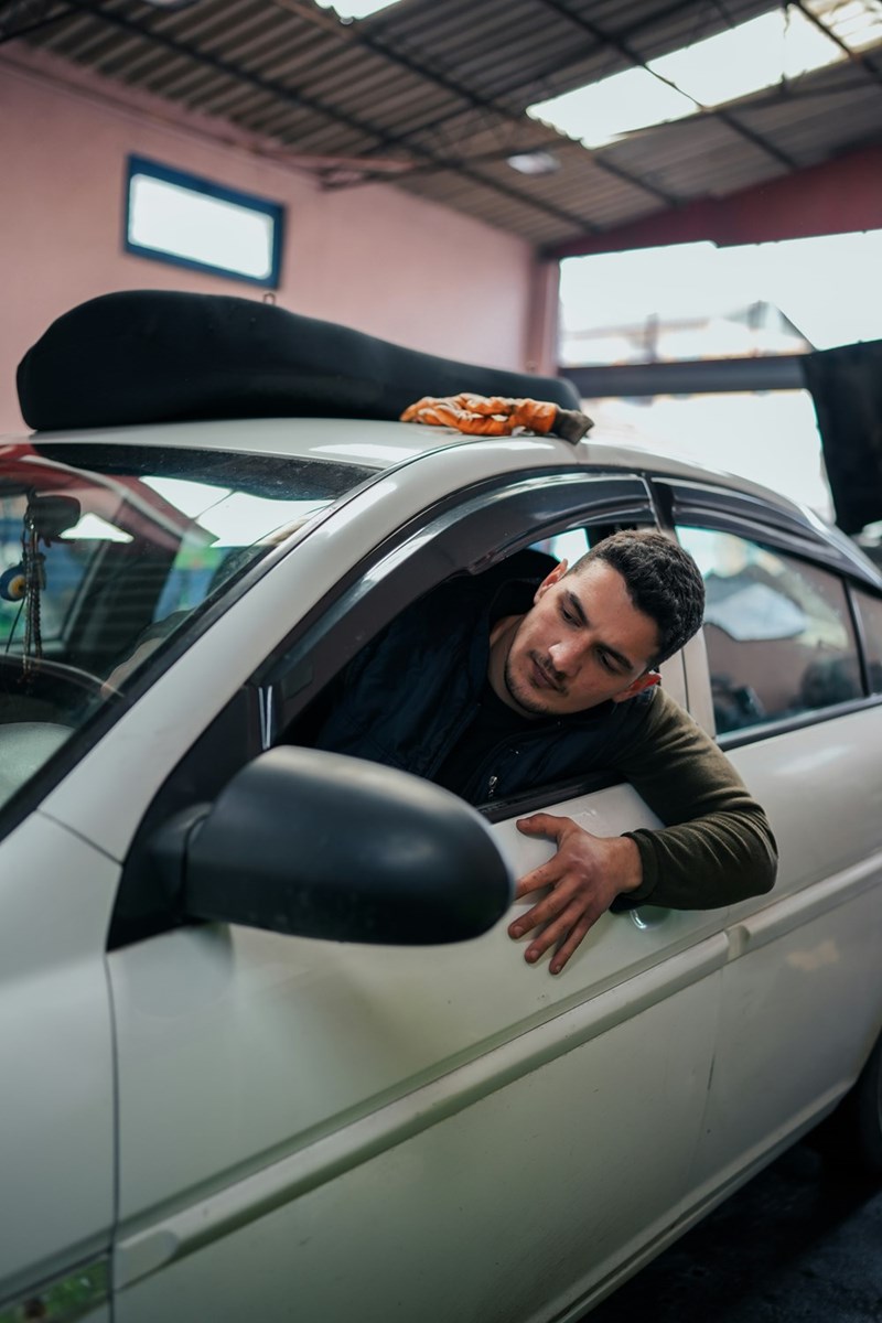 Man sitting in his car parked in a parking lot looking outside his window.