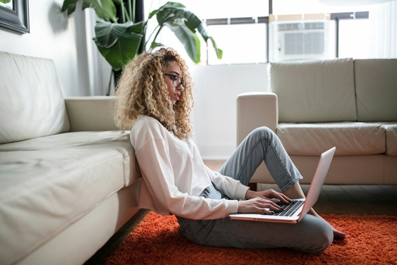 A woman works remotely beside a shared apartment couch in an illustrative image about roommate conflict and remote work boundaries.