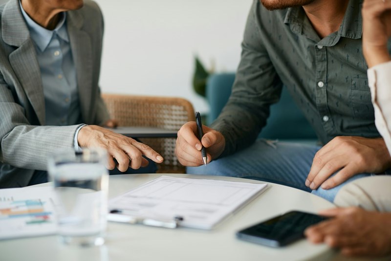 A close-up representative image of three people closing a deal and signing paperwork.