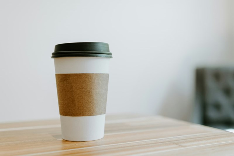 A simple to-go coffee cup sits atop a wooden table for a photograph.