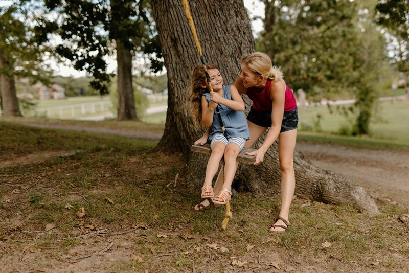 Mom and daughter spend time other, as the Mother pushes her child on a swing.